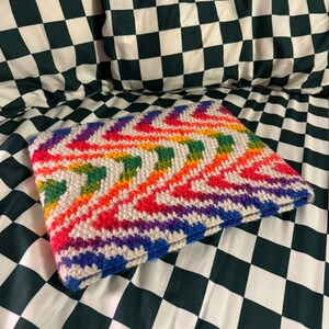 May include: A rainbow chevron crochet blanket with a white background. The blanket is lying on a black and white checkered surface.