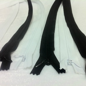 May include: A close-up of two white and two black zipper tapes. The zippers are open and the slider pulls are visible.