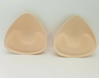 Puede incluir: Dos insertos de sujetador triangulares de color beige con una superficie texturizada.