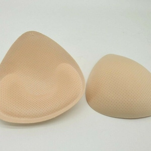 Puede incluir: Dos insertos de sujetador beige, uno más grande que el otro, con una textura punteada.