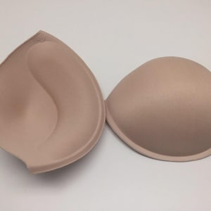 May include: Two beige bra inserts, one with a curved shape and the other with a rounded shape.