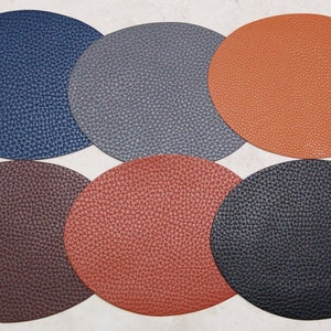 Puede incluir: Seis manteles individuales redondos de cuero en varios colores, incluyendo azul marino, gris, naranja, marrón y negro.