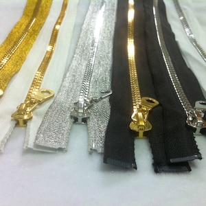 May include: Assortment of five zipper closures in different colors and finishes. The zippers are gold, silver, black, and white. The zippers are all closed and have a metal slider.