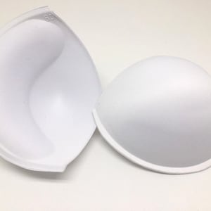 May include: Two white foam bra inserts. The inserts are shaped like half a sphere and have a smooth, rounded surface. The insert on the left has the number "80" printed on it.