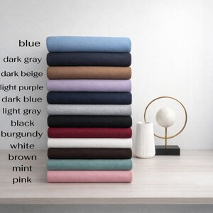 May include: A stack of folded fabric in various colors, including blue, dark gray, and pink. The image includes text labels for each color. A decorative gold and white sculpture is in the background.