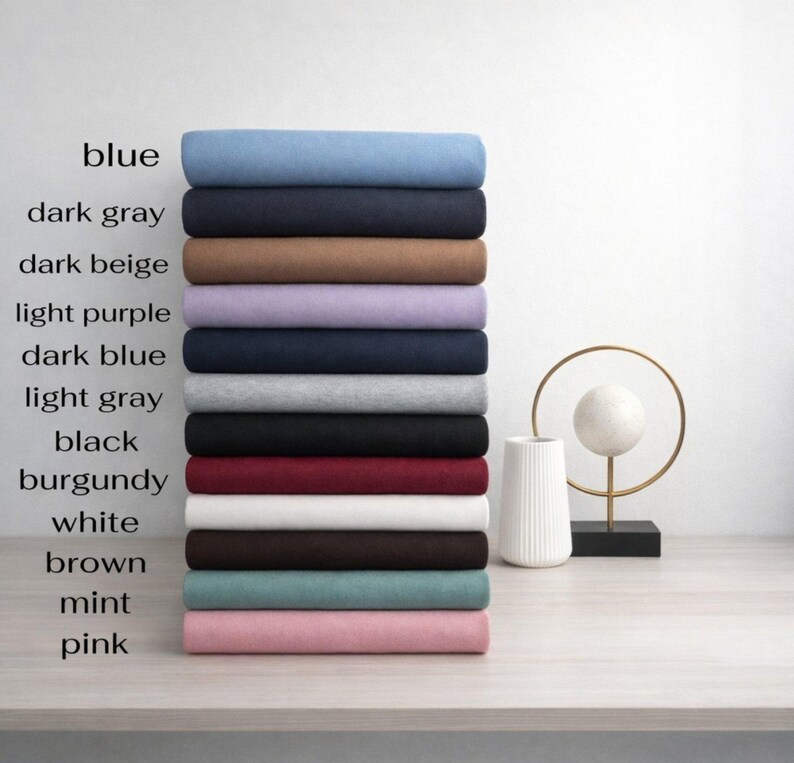 May include: A stack of folded fabric in various colors, including blue, dark gray, and pink. The image includes text labels for each color. A decorative gold and white sculpture is in the background.