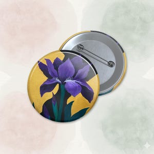 Könnte beinhalten: Zwei runde Ansteckbuttons. Ein Button zeigt eine lila Irisblüte mit grünen Blättern vor goldenem Hintergrund. Der andere Button zeigt die silberne Anstecknadel. Die Buttons haben wahrscheinlich einen Durchmesser von 3,8 cm.