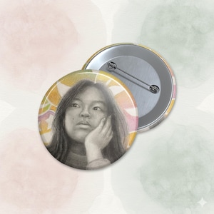 Puede incluir: Un botón redondo con un boceto a lápiz de una persona pensativa. El fondo del botón tiene un diseño abstracto y colorido. La parte posterior del botón es plateada con un alfiler.