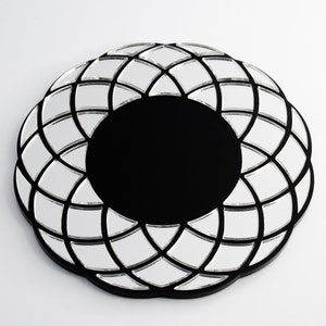 May include: A round decorative mirror with a black frame and a unique design. The mirror features a central black circle surrounded by a pattern of small, mirrored squares. The overall shape is reminiscent of a flower or sunburst.