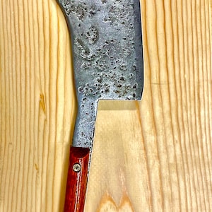May include: A vintage cleaver with a wooden handle. The blade is made of metal and has a worn, rustic look. The handle is a dark reddish brown color.