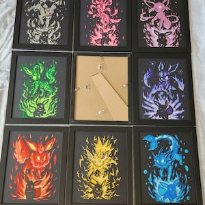 May include: Nine framed prints of Pokemon characters, each with a different colour background and a different Pokemon character. The characters are Eevee, Flareon, Jolteon, Vaporeon, Espeon, Umbreon, Leafeon, Glaceon, and Sylveon.