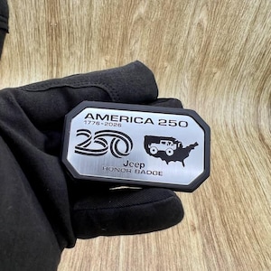 May include: A rectangular metal badge with a black border featuring the text AMERICA 250, 1776-2026, a stylized 250 graphic, a silhouette of the United States with a Jeep vehicle icon, and the text Jeep HONOR BADGE in black lettering.