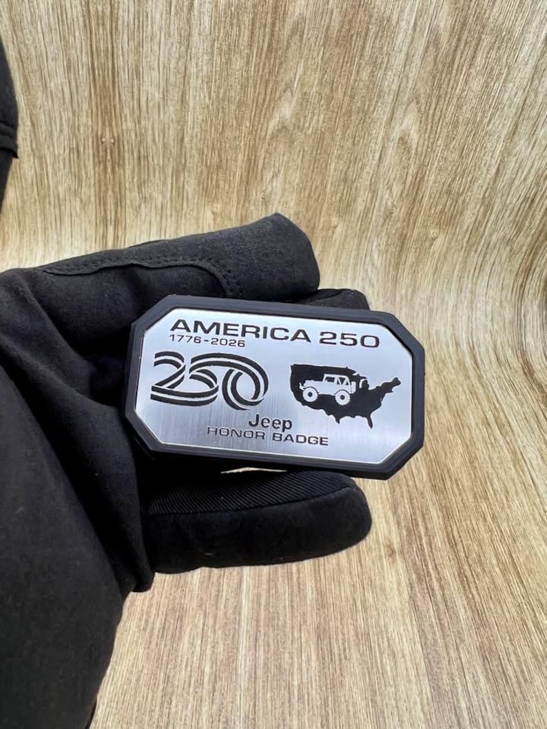 May include: A rectangular metal badge with a black border featuring the text AMERICA 250, 1776-2026, a stylized 250 graphic, a silhouette of the United States with a Jeep vehicle icon, and the text Jeep HONOR BADGE in black lettering.