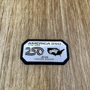 May include: A rectangular silver metal badge with a black border featuring the text AMERICA 250, 1776-2026, a stylized 250 logo, a silhouette of the United States with a Jeep vehicle icon, and the text Jeep HONOR BADGE printed in black.