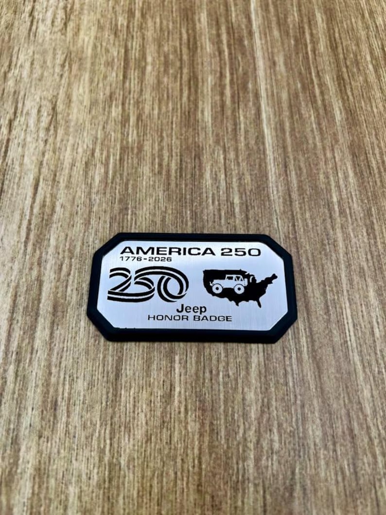May include: A rectangular silver metal badge with a black border featuring the text AMERICA 250, 1776-2026, a stylized 250 logo, a silhouette of the United States with a Jeep vehicle icon, and the text Jeep HONOR BADGE printed in black.
