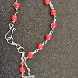 May include: A red beaded bracelet with a silver cross charm. The bracelet is made with wire and red beads.