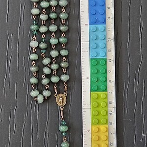 K&ouml;nnte beinhalten: Ein Rosenkranz mit gr&uuml;nen Perlen und kupferfarbenem Draht. Der Rosenkranz ist etwa 28 cm lang. Er hat ein Kruzifix und ein kleines Medaillon. Die Perlen sind hellgr&uuml;n.