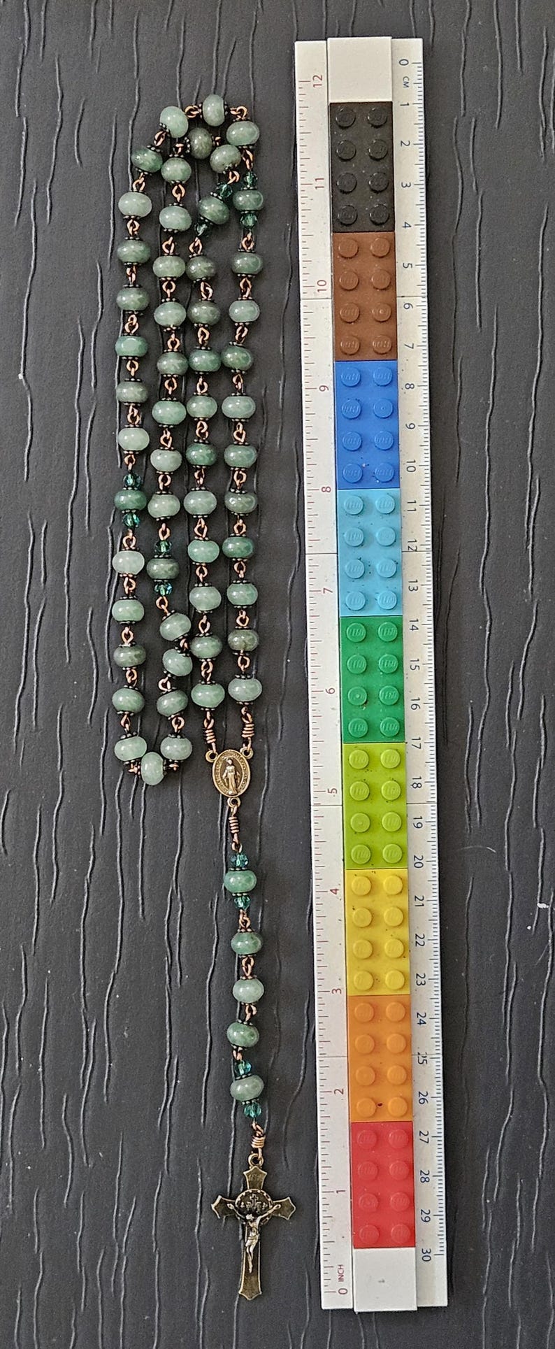 K&ouml;nnte beinhalten: Ein Rosenkranz mit gr&uuml;nen Perlen und kupferfarbenem Draht. Der Rosenkranz ist etwa 28 cm lang. Er hat ein Kruzifix und ein kleines Medaillon. Die Perlen sind hellgr&uuml;n.