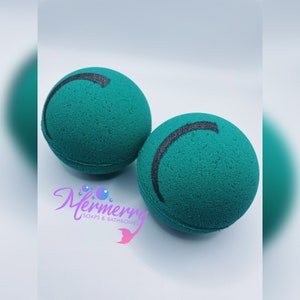Puede incluir: Dos bombas de baño verdes con un diseño de línea curva negra. Las bombas de baño son redondas y tienen una superficie texturizada.