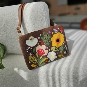 May include: A brown fabric handbag with a long strap. The bag has a floral embroidery design with yellow, pink, white, and green flowers.