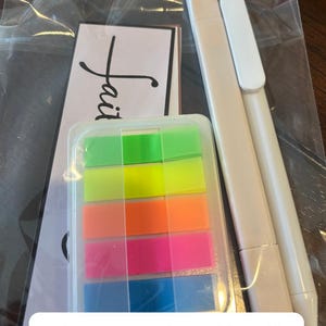 May include: A Bible annotation kit in a clear plastic bag containing a white highlighter, a white pen, a rectangular case with five neon-colored adhesive page markers in green, yellow, orange, pink, and blue, and a card with the word faith.