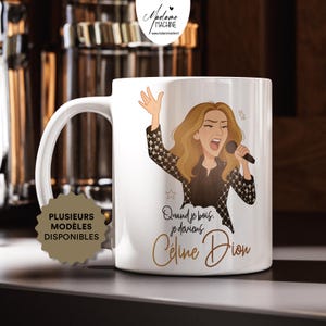 May include: White ceramic mug featuring a cartoon illustration of a singer with long blonde hair, holding a microphone. The mug has the text "Quand je bois, je deviens Céline Dion" in gold script. The mug also has the text "PLUSIEURS MODELES DISPONIBLES".