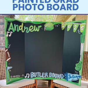May include: A tri-fold black display board with hand-painted green borders and illustrations including a football, golf clubs, and musical notes. The text reads Andrew, 2026, Go Vikings!, Butler Bound, and Go Dawgs in white and blue lettering.
