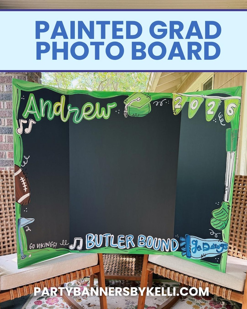 May include: A tri-fold black display board with hand-painted green borders and illustrations including a football, golf clubs, and musical notes. The text reads Andrew, 2026, Go Vikings!, Butler Bound, and Go Dawgs in white and blue lettering.