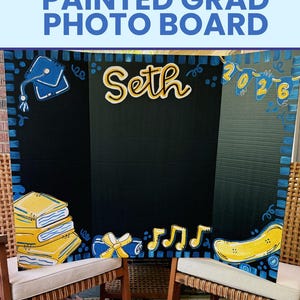 May include: A black tri-fold display board featuring hand-painted yellow and blue graduation-themed illustrations. The board displays the name Seth, a graduation cap, a stack of books, musical notes, a skateboard, and the year 2026.