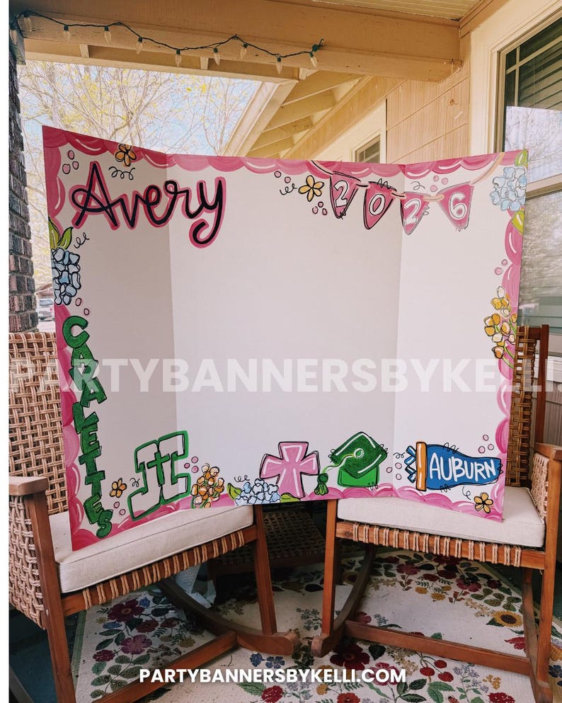 May include: A white tri-fold display board featuring hand-painted pink scalloped borders, floral accents, and the name Avery in black script. It includes the year 2026 on pink pennants, the word CARALETTES in green, and the text AUBURN in blue.