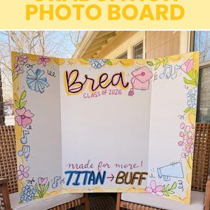 May include: A tri-fold white graduation photo board featuring hand-drawn illustrations of flowers, musical notes, a megaphone, and a graduation cap. The text reads Brea Class of 2026 and made for more! TITAN to BUFF in colourful lettering.