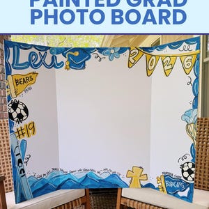May include: A white tri-fold display board featuring hand-painted blue and yellow designs. The board includes the name Lexi, a graduation cap, a 2026 banner, a football, the number 19, a cross, and the text Montana State Bobcats.