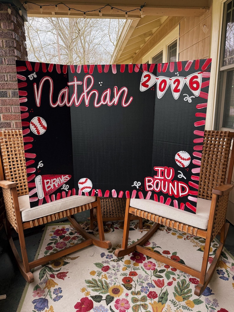 May include: A black tri-fold display board featuring hand-painted red and pink baseball-themed decorations. The board displays the name Nathan, the year 2026 on a banner, a pennant labelled Braves, and the text IU BOUND with baseball illustrations.