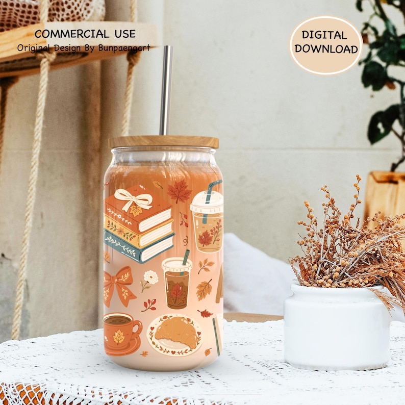 May include: A clear glass tumbler with a bamboo lid and a metal straw, featuring a wrap-around print of autumn-themed illustrations including stacked books, iced coffee cups, a warm mug, a croissant, and fall leaves in orange, blue, and white.