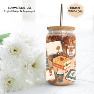 May include: A glass tumbler with a bamboo lid and a metal straw, featuring a printed design of open books, a vase with autumn leaves, and a cup of coffee. The text on the books includes the phrase Just One More Chapter in a fall color palette.