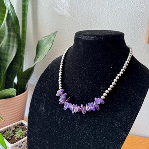 May include: A silver chain necklace with a cluster of purple amethyst stones.
