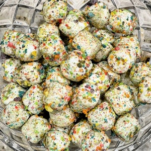 May include: A glass bowl filled with white marshmallow squares covered in colorful sprinkles. The sprinkles are a mix of red, green, yellow, and blue.
