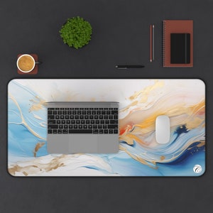 Puede incluir: Alfombrilla de escritorio rectangular con un diseño abstracto en tonos azules, blancos y dorados. Hay un portátil, un ratón, un bolígrafo, un cuaderno y una pequeña planta sobre la alfombrilla. Una taza de café está sobre un posavasos.