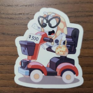May include: A sticker featuring a cartoon dog wearing glasses and riding a red and black mobility scooter. The scooter has a basket and a small purse hanging from the back. The sticker has the text "$300" on the scooter.