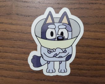 Könnte beinhalten: Ein Aufkleber mit einer Cartoon-Hundefigur mit hellblauem Körper, dunkelblauen Flecken und einem hellgelben Kegel. Der Hund hat große schwarze Augen und lächelt. Der Aufkleber ist schwarz umrandet.