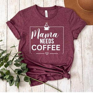 May include: Burgundy t-shirt with a white graphic that says "Mama Needs Coffee" with a small coffee cup icon and a heart.