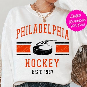 May include: White sweatshirt with a red and black graphic design that says "PHILADELPHIA HOCKEY EST. 1967" with a black hockey puck graphic.