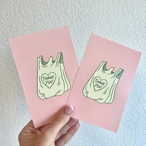 May include: Two pink cards featuring a green outline of a plastic shopping bag with a heart that says "Thank You!" on it.