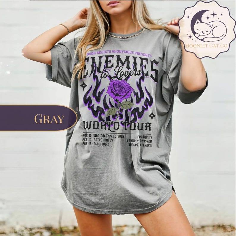 May include: Grey oversized t-shirt with the text "Enemies to Lovers World Tour" featuring a purple rose and flames graphic. The shirt lists tour dates and artist names. The shirt has a relaxed fit.