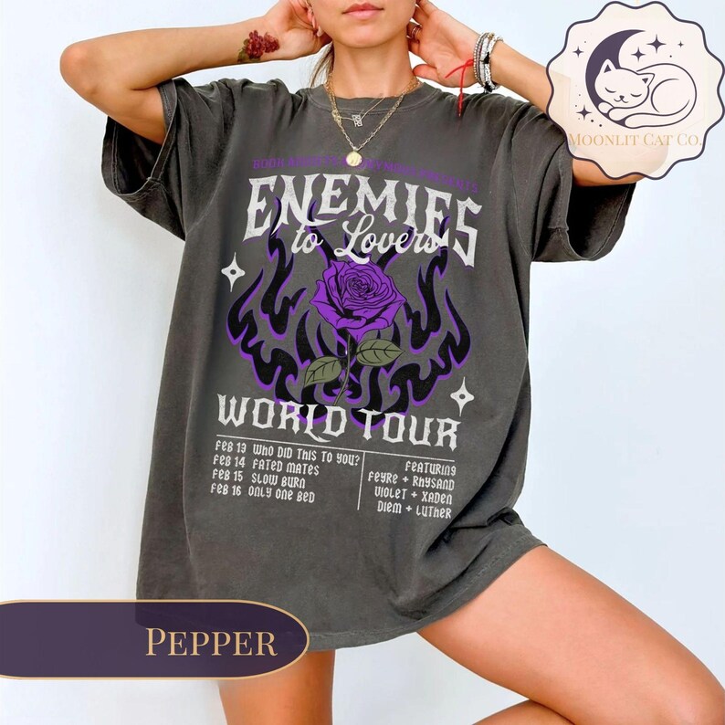 May include: A pepper-coloured graphic tee with the text "Enemies to Lovers World Tour", a purple rose, and flame design. The tee lists tour dates and featured artists. A Moonlit Cat Co. logo is visible.