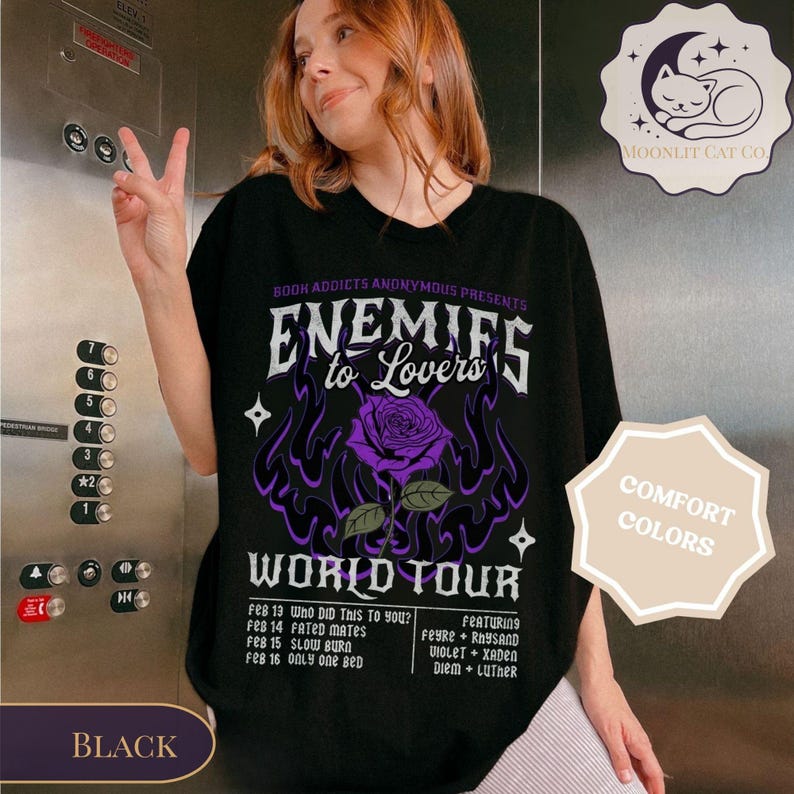 May include: Black t-shirt with a graphic design featuring the text "ENEMIES to Lovers" and a purple rose. The shirt also includes tour dates and the words "WORLD TOUR". The shirt is labeled "COMFORT COLORS".