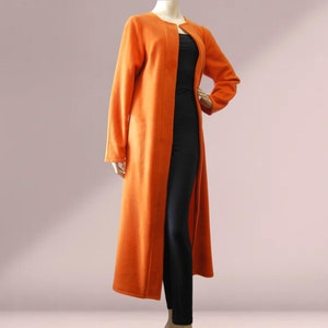 May include: An orange longline cardigan with long sleeves. The open-front cardigan is displayed on a mannequin, revealing a black outfit underneath. The cardigan's length extends to the ankles.