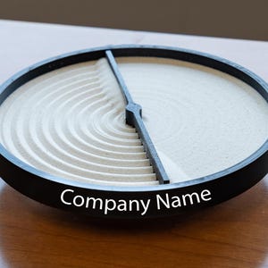 May include: A black circular tray with a white sand design divided in half. The tray has the text "Company Name" printed on the bottom.