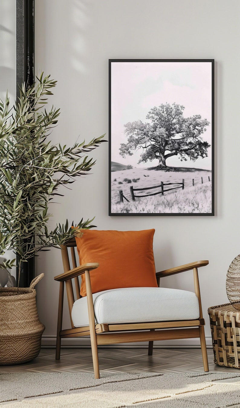 May include: A black and white photograph of a lone tree in a field with a wooden fence in the foreground. The tree is in the center of the image and is surrounded by grass. The fence is made of horizontal wooden rails and is in the lower right corner of the image.