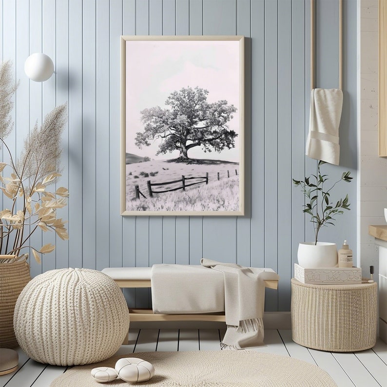 May include: A black and white photograph of a lone tree in a field with a wooden fence. The photo is framed in a light wood frame and hanging on a light blue wall.